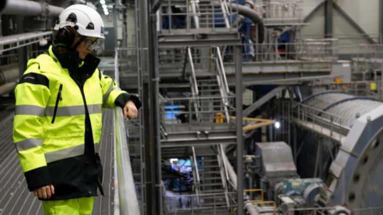 A person wearing a yellow jacket and a white helmet in an industrial building